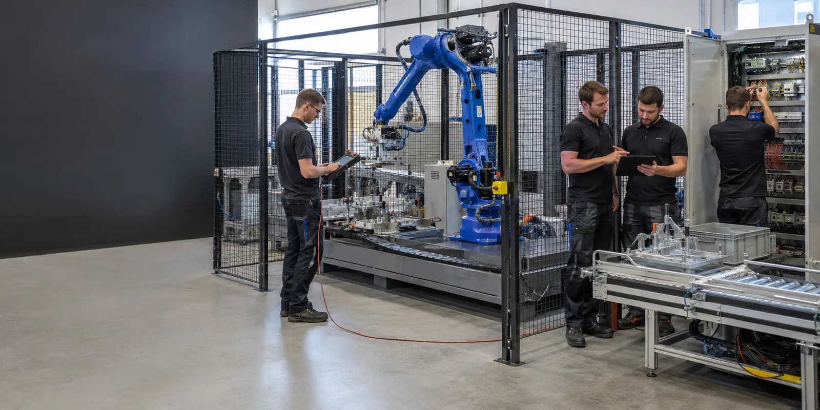 Techniker nehmen eine blaue Roboterzelle in einer Integrationswerkstatt in Betrieb